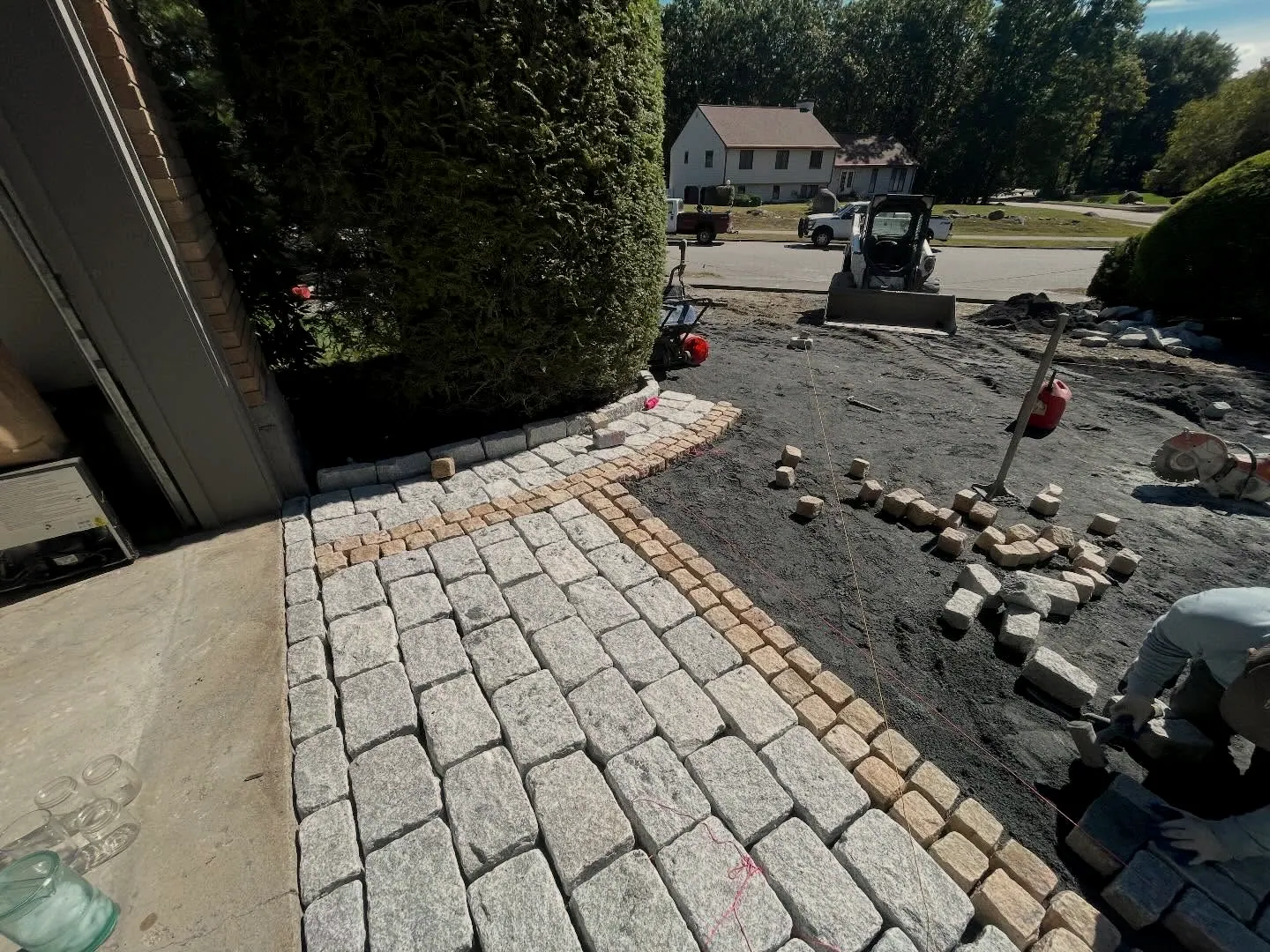 Granite cobblestone driveway apron being set with a tan cobble accent band, skid steer behind