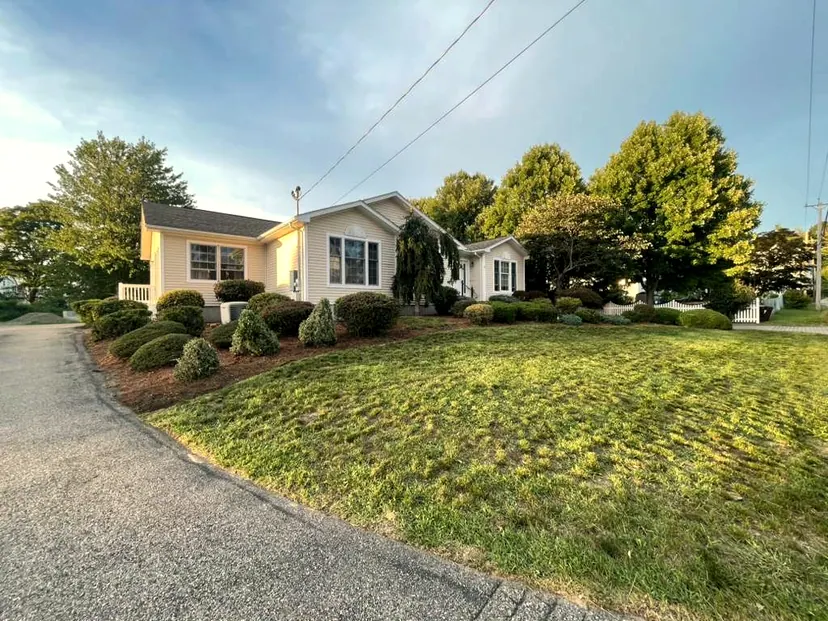 Corner-lot ranch house with a mowed lawn, trimmed rounded shrubs and mulch beds