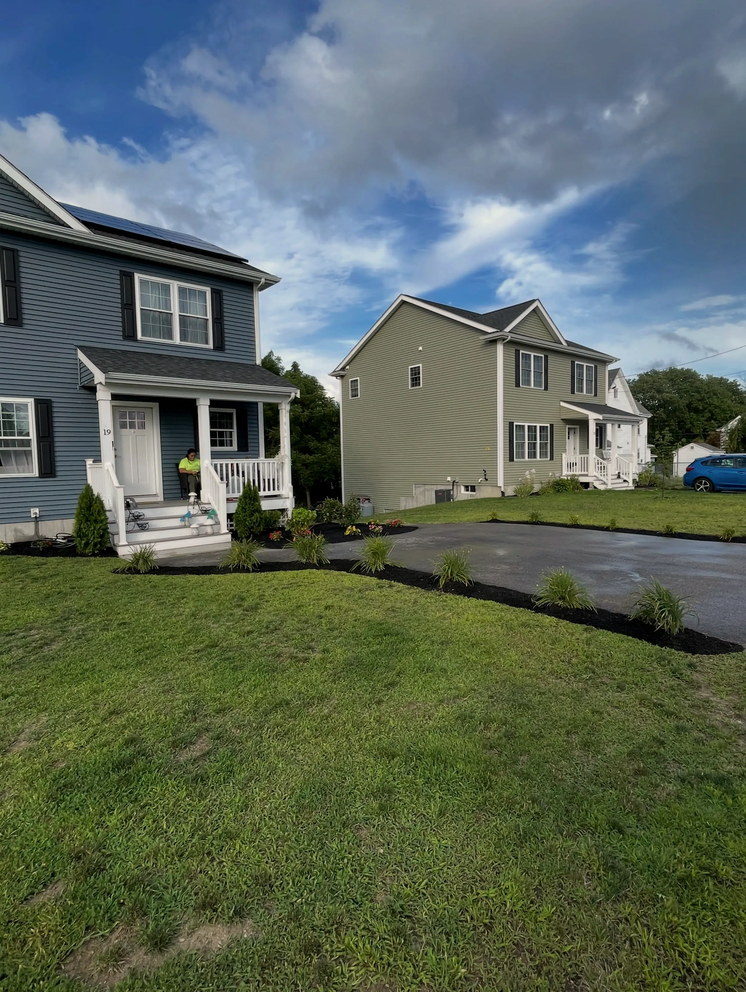 New lawn and black-mulch beds along a driveway in front of two houses