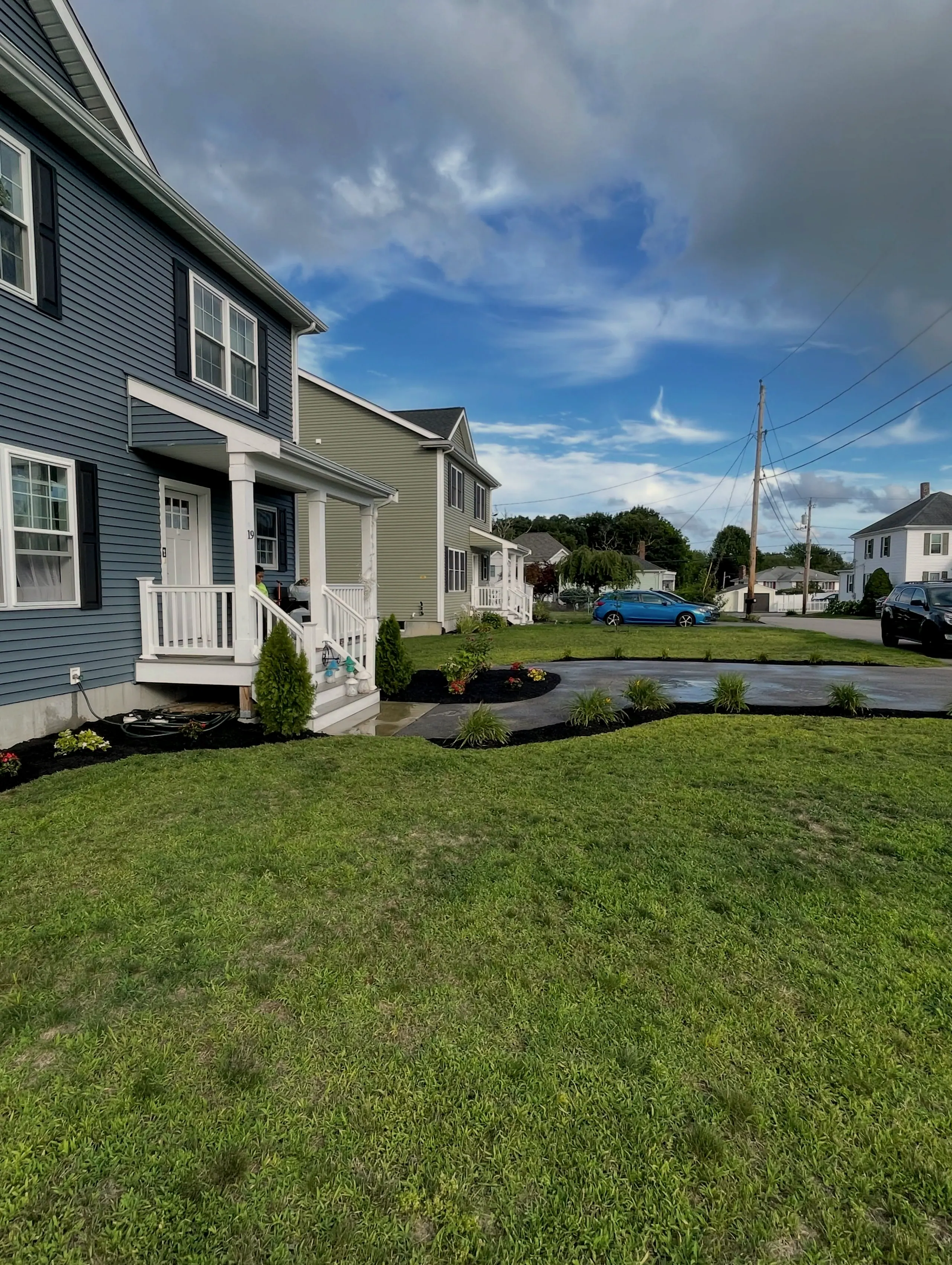 Front lawn of a blue house with new planting beds along the walkway and driveway under a blue sky