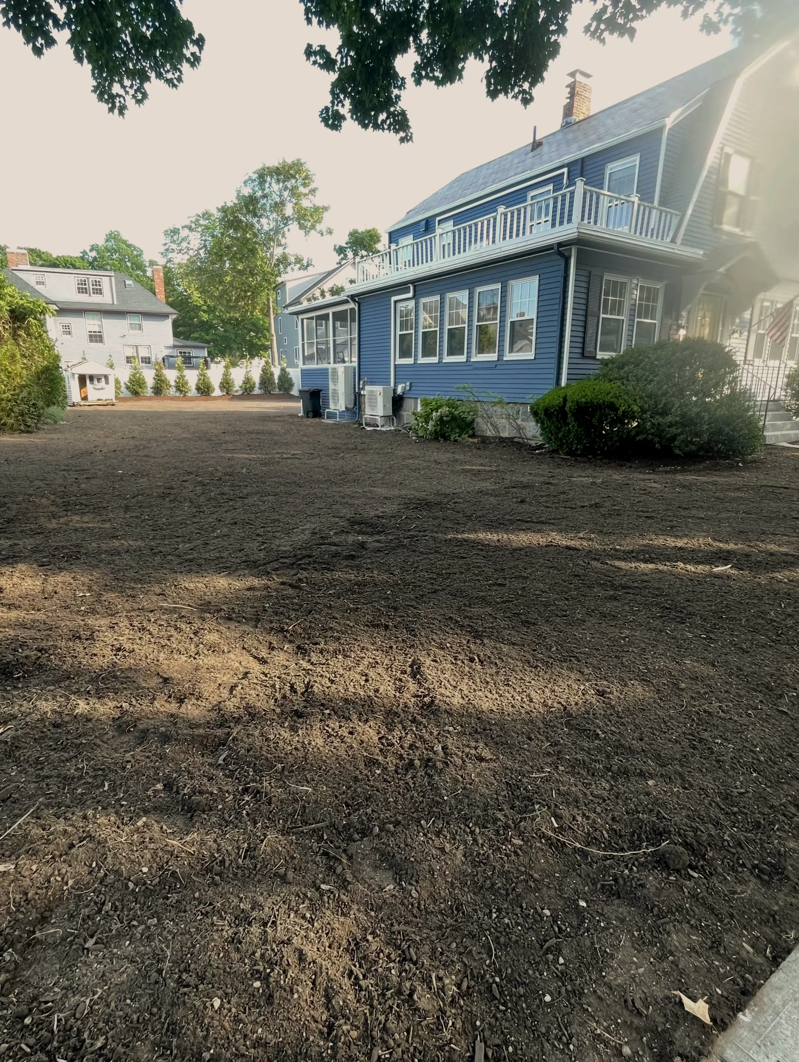 Graded side yard of bare loam beside a blue house, wider view